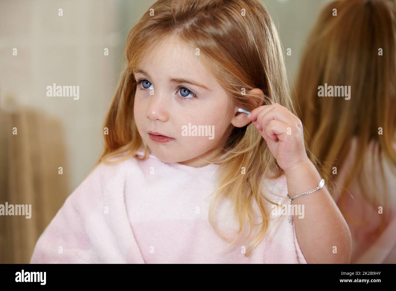 Sicherstellen, dass sie richtig reinigt. Nettes kleines Mädchen, das ihre Ohren mit einem Ohrstöpsel putzt. Stockfoto