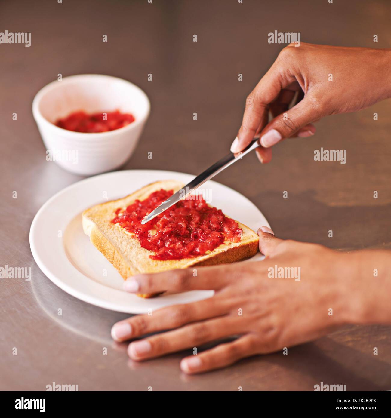 Fruchtiger Genuss zum Frühstück. Kurzer Schuss einer Frau, die fruchtige Marmelade auf Toast verteilt. Stockfoto