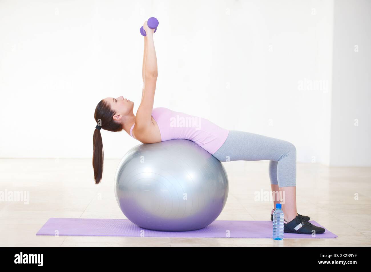 Balance und Kraft. Ganzkörperaufnahme einer jungen Frau, die auf einem Übungsball zurückliegt und Gewichte hebt. Stockfoto