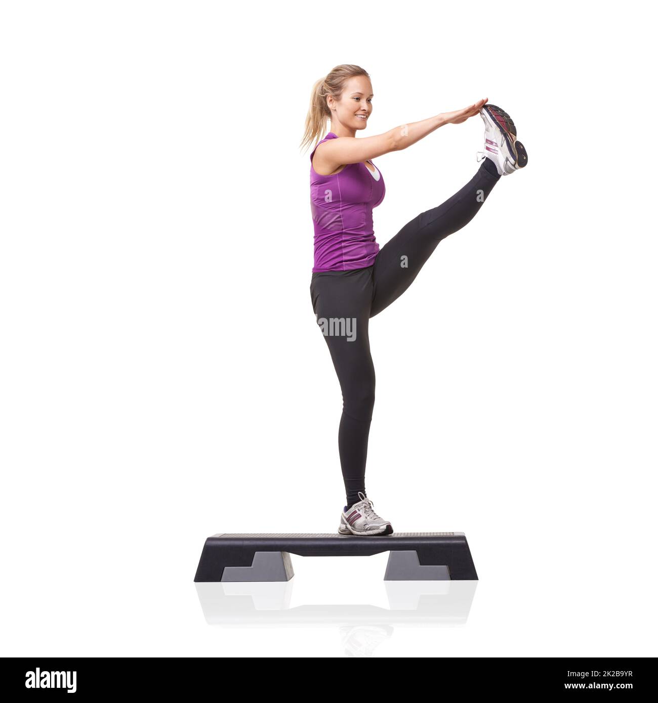 Flexibel und fit. Eine lächelnde junge Frau macht Aerobic auf einem Aerobic-Schritt vor einem weißen Hintergrund. Stockfoto