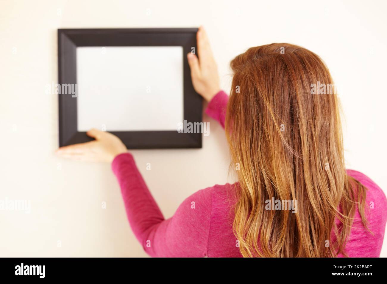Perfekt im Bild. Rückansicht einer Frau, die einen leeren Rahmen an eine Wand legt. Stockfoto
