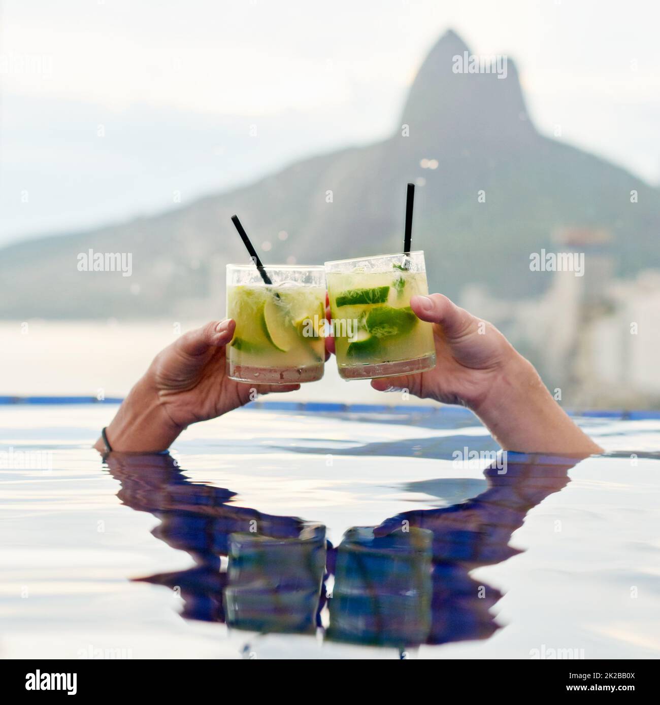 Heres zu einer wunderbaren Aussicht. Zugeschnittene Aufnahme von zwei Personen, die in einem Pool mit Aussicht toasten. Stockfoto