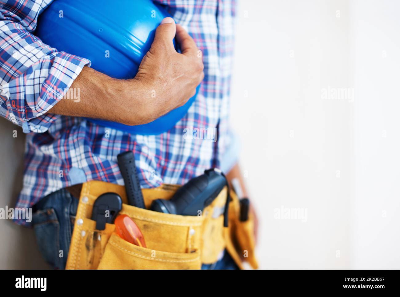 Bauarbeiter mit Schutzhelm. Mittlerer Abschnitt des Bauarbeiters mit Werkzeuggurt, der den blauen Schutzhelm hält. Stockfoto