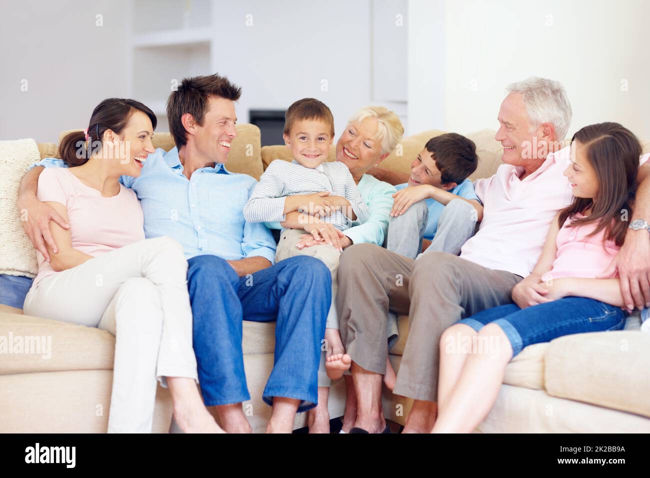 Drei Generationen versammeln sich glücklich zusammen. Drei Generationen Familie sitzen liebevoll auf der Loungecouch zusammen. Stockfoto