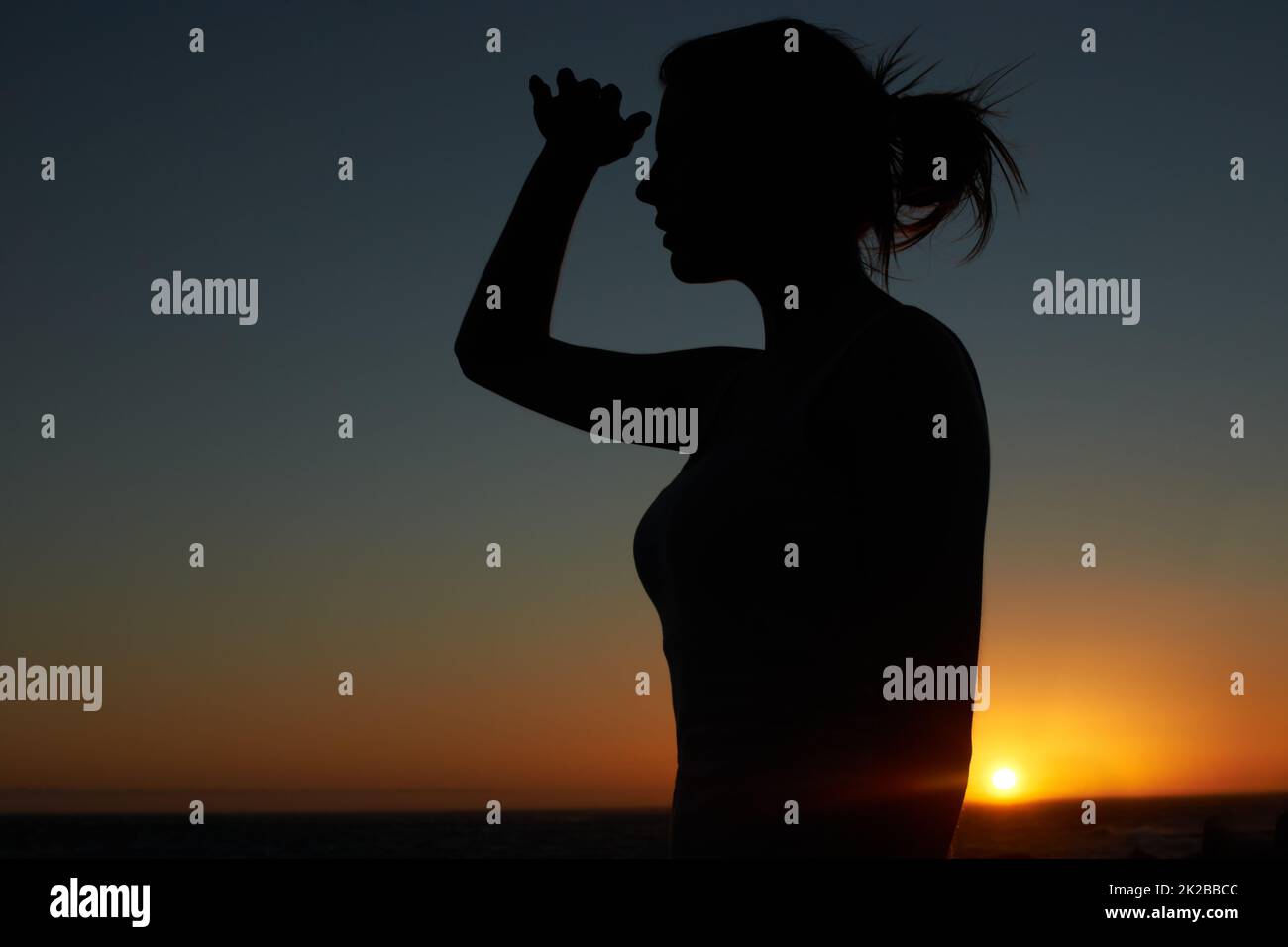 So weit das Auge reicht. Silhouette einer jungen Frau, die in die Ferne blickt, gegen eine untergehende Sonne. Stockfoto