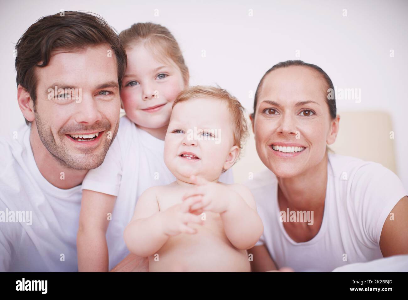 Unsere schöne Familie. Beschnittenes Porträt einer liebevollen Familie mit zwei Kindern, die zusammen in einem Schlafzimmer sitzen. Stockfoto