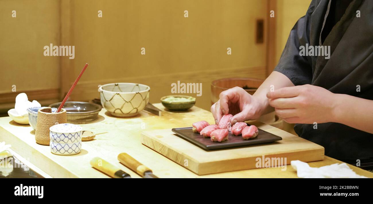 Der Küchenchef legt Thunfisch-Sushi auf schwarzen Keramikteller. Stockfoto