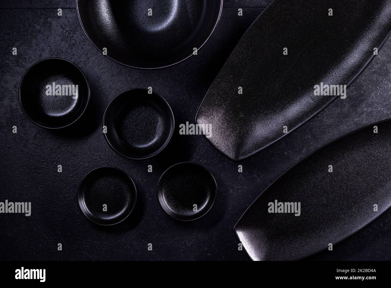 Schwarze Teller und Schüsseln auf schwarzem Hintergrund Stockfoto