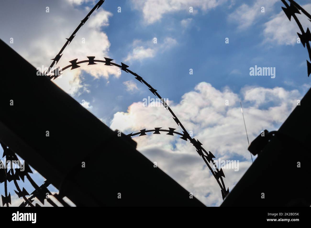 Stacheldraht an einem wolkigen Himmel auf einem großen Zaun an einer Grenze. Stockfoto