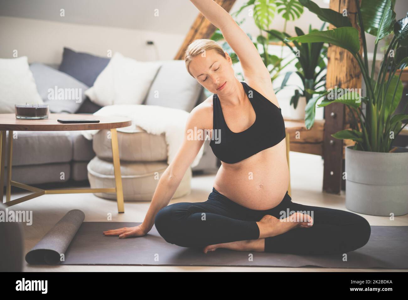 Junge schöne Schwangerin, die zu Hause in ihrem Wohnzimmer Yoga trainiert. Mutterschaft, Schwangerschaft, gesunder Lebensstil und Yoga-Konzept Stockfoto