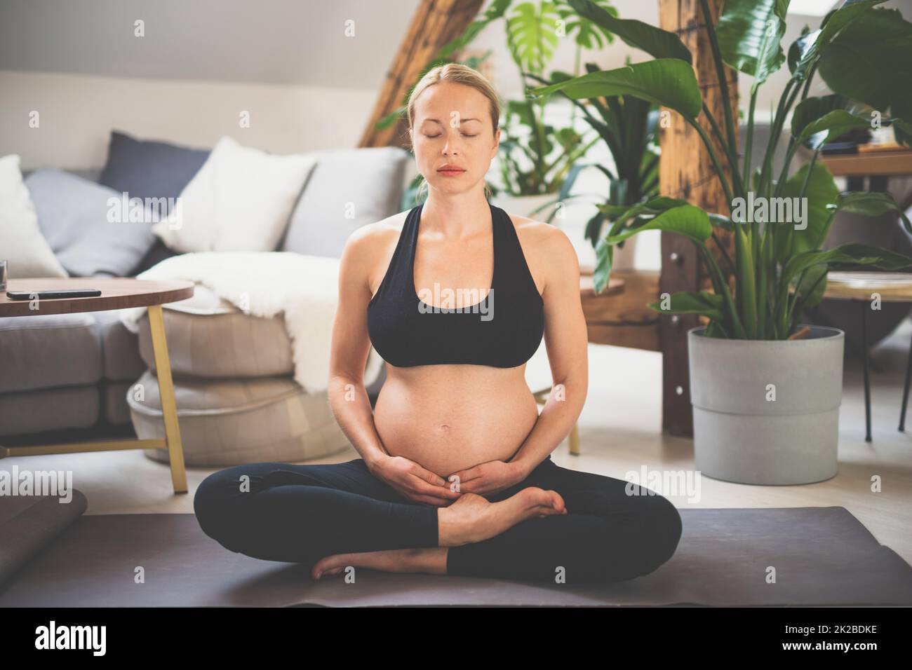 Junge, schöne, schwangere Frau, die Yoga trainiert, ihren Bauch streichelt. Junge, fröhlich, erwartungsvoll, entspannt, denkt an ihr Baby und genießt ihr zukünftiges Leben. Mutterschaft, Schwangerschaft, Yoga-Konzept. Stockfoto
