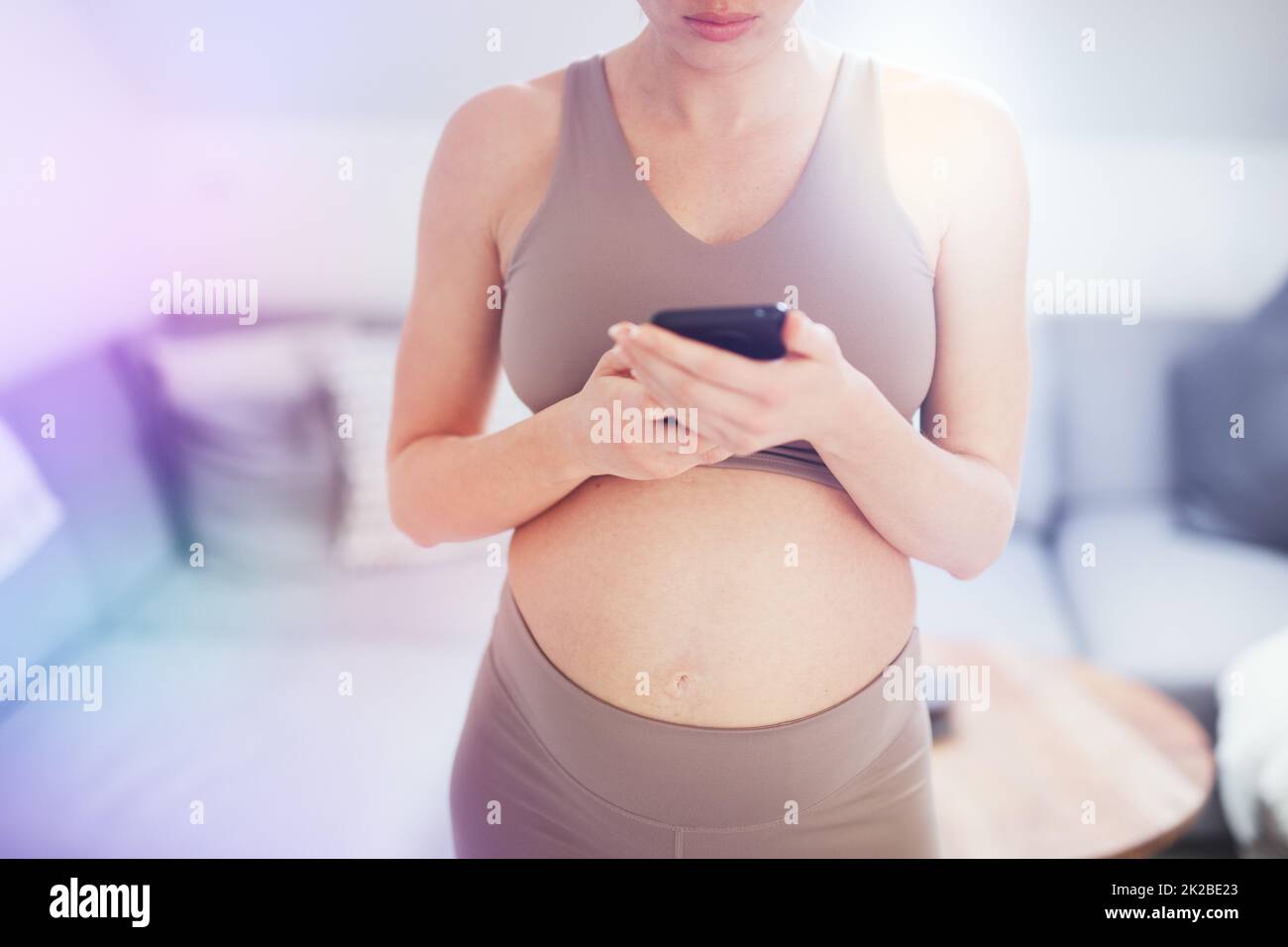 Nahaufnahme des schwangeren weiblichen Bauches. Frau, die eine Smartphone-App in der Wohnung hält und verwendet. Schwangerschaft, Technologie, Online-Shopping, Vorbereitung und Erwartungskonzept. Stockfoto
