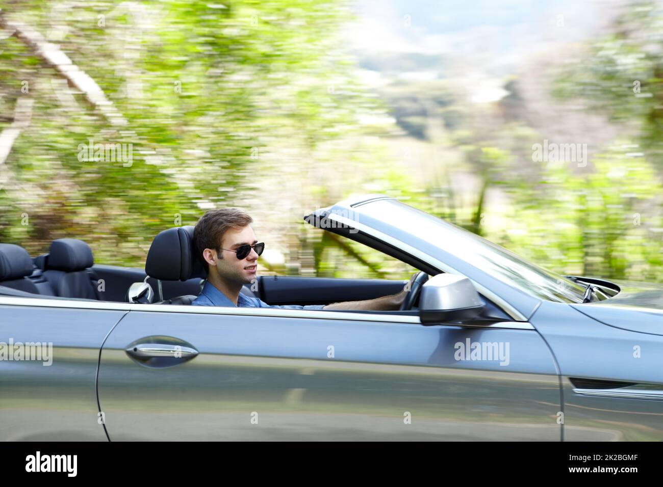 Er liebt sein Cabrio. Ein junger Mann, der ein silbernes konvertierbares Fahrzeug fährt. Stockfoto