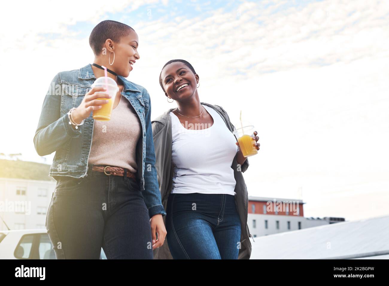 Gemeinsam mit Ihnen durch jeden Lebensabschnitt. Aufnahme zweier junger Frauen, die in der Stadt lachen und dabei ihre kühlen Getränke halten. Stockfoto