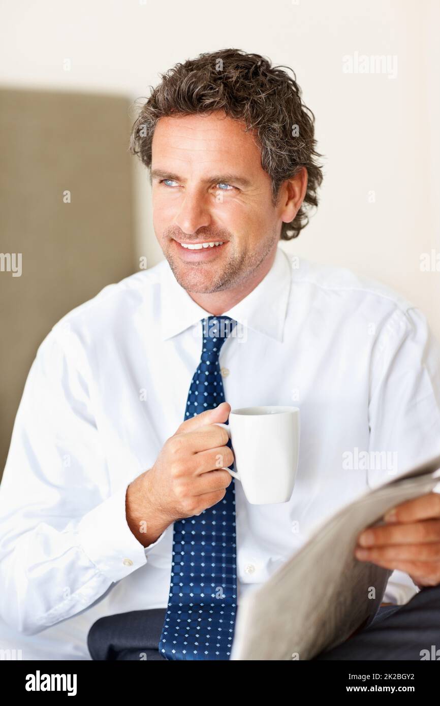 Geschäftsmann mit einer Tasse Kaffee und Zeitung. Ein hübscher Geschäftsmann mit einer Tasse Kaffee und einer Zeitung, der lächelt und wegschaut. Stockfoto