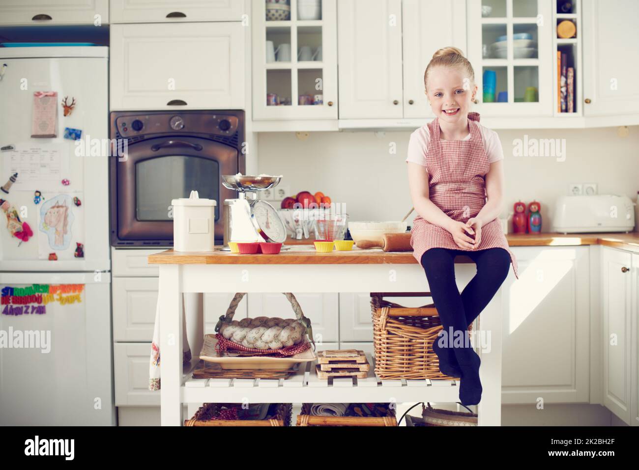 Bereit, einige Backkünste zu erlernen. Niedliches kleines Mädchen, das auf der Küchentheke sitzt und mit dem Backen beginnt. Stockfoto