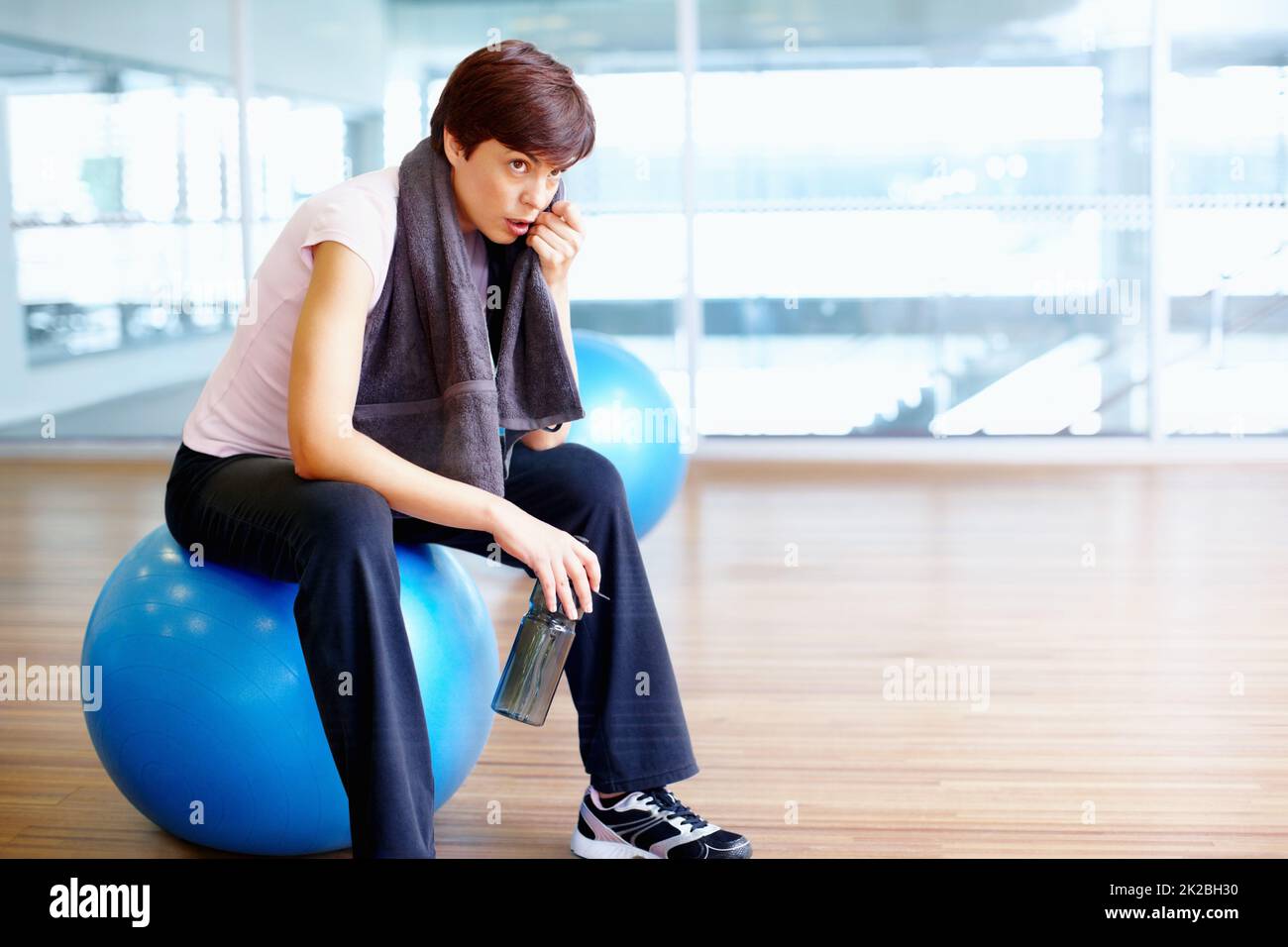 Atempause. Frau, die auf einem Pilates-Ball sitzt und mit einem Handtuch Schweiß abwischt. Stockfoto