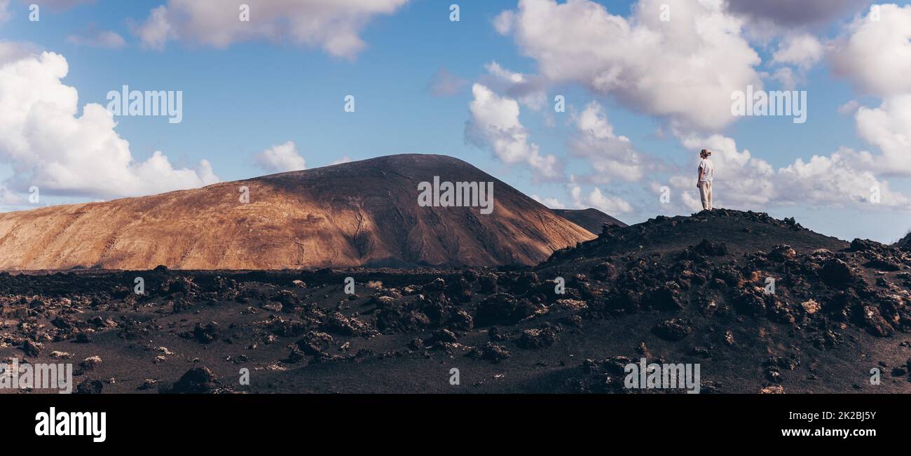 Eine Frau erhebt sich in den Himmel und genießt den fantastischen Blick auf die vulkanische Landschaft im Nationalpark Timanfaya auf Lanzarote, Spanien. Freiheit und Abenteuerkonzept. Stockfoto