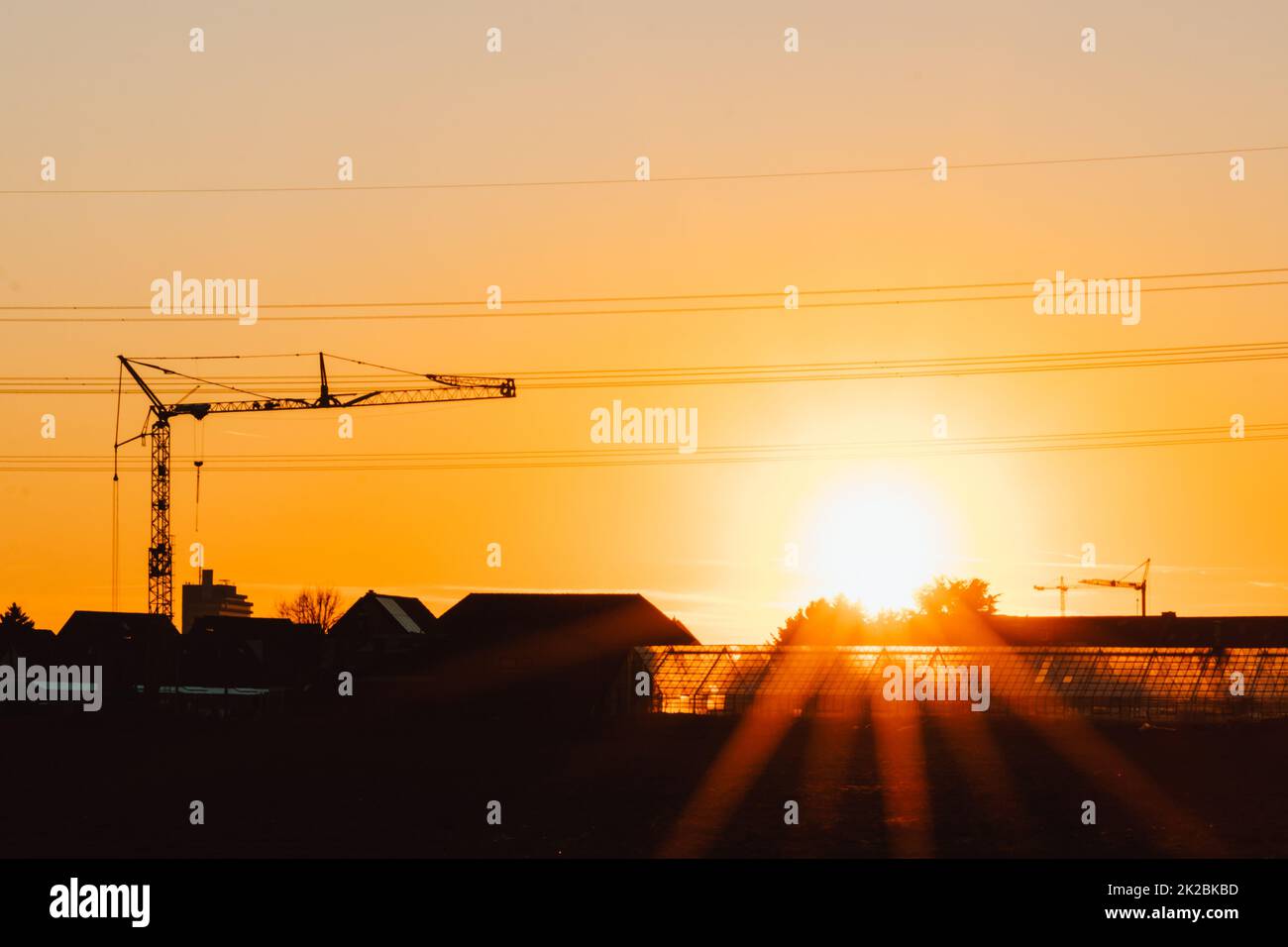 Die Silhouette eines hohen Baukrans in Orange zeigt den Sonnenuntergang auf der Baustelle mit Bauarbeiten für moderne Gebäude und Stadtentwicklung als architektonisches Teamwork für Hochspannungsleitungen von Wolkenkratzern Stockfoto