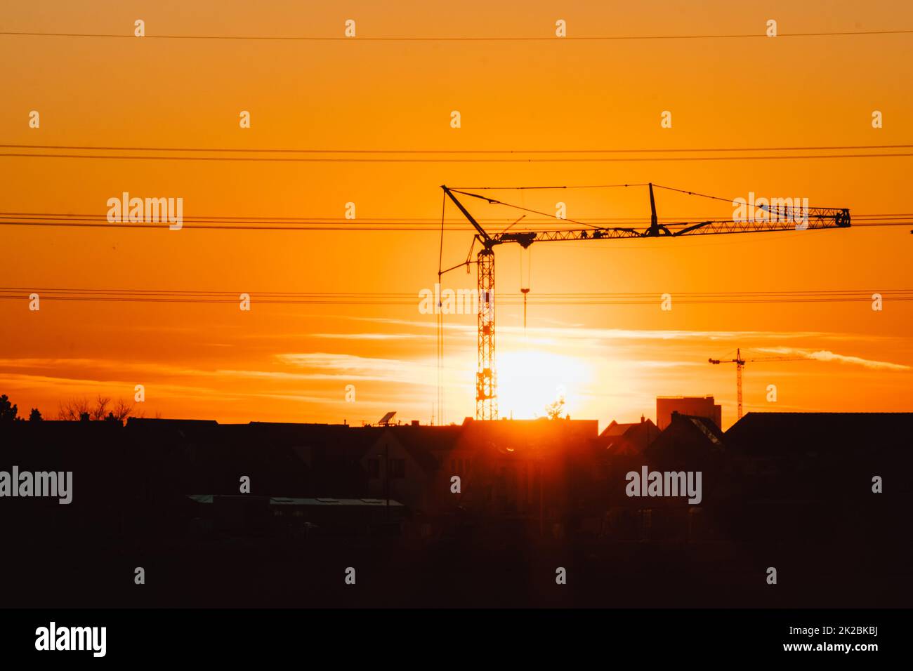 Die Silhouette eines hohen Baukrans in Orange zeigt den Sonnenuntergang auf der Baustelle mit Bauarbeiten für moderne Gebäude und Stadtentwicklung als architektonisches Teamwork für Hochspannungsleitungen von Wolkenkratzern Stockfoto