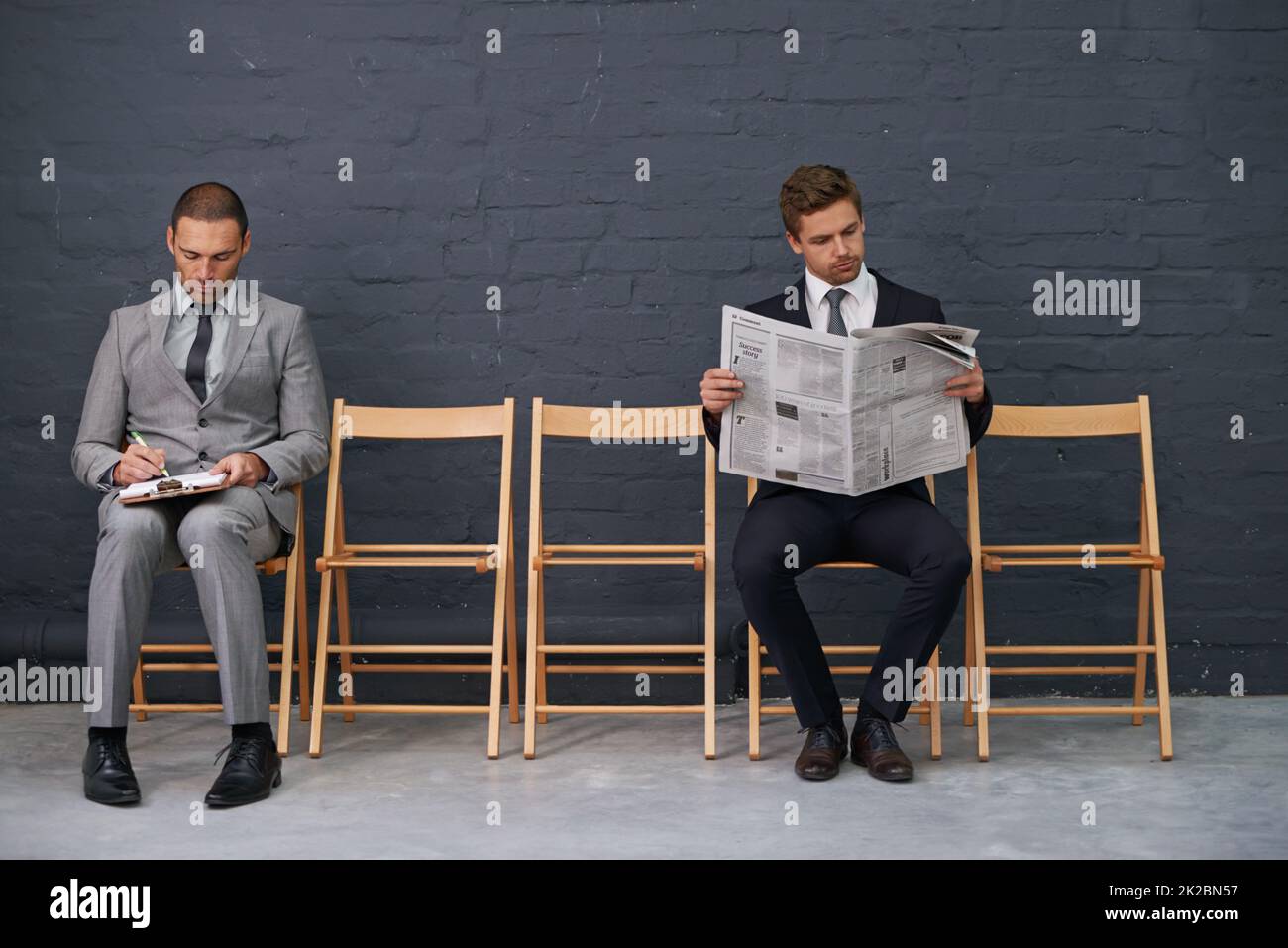 Trennung der Konkurrenz. Aufnahme einer Stuhlreihe mit zwei leicht auseinander sitzenden Geschäftsleuten. Stockfoto