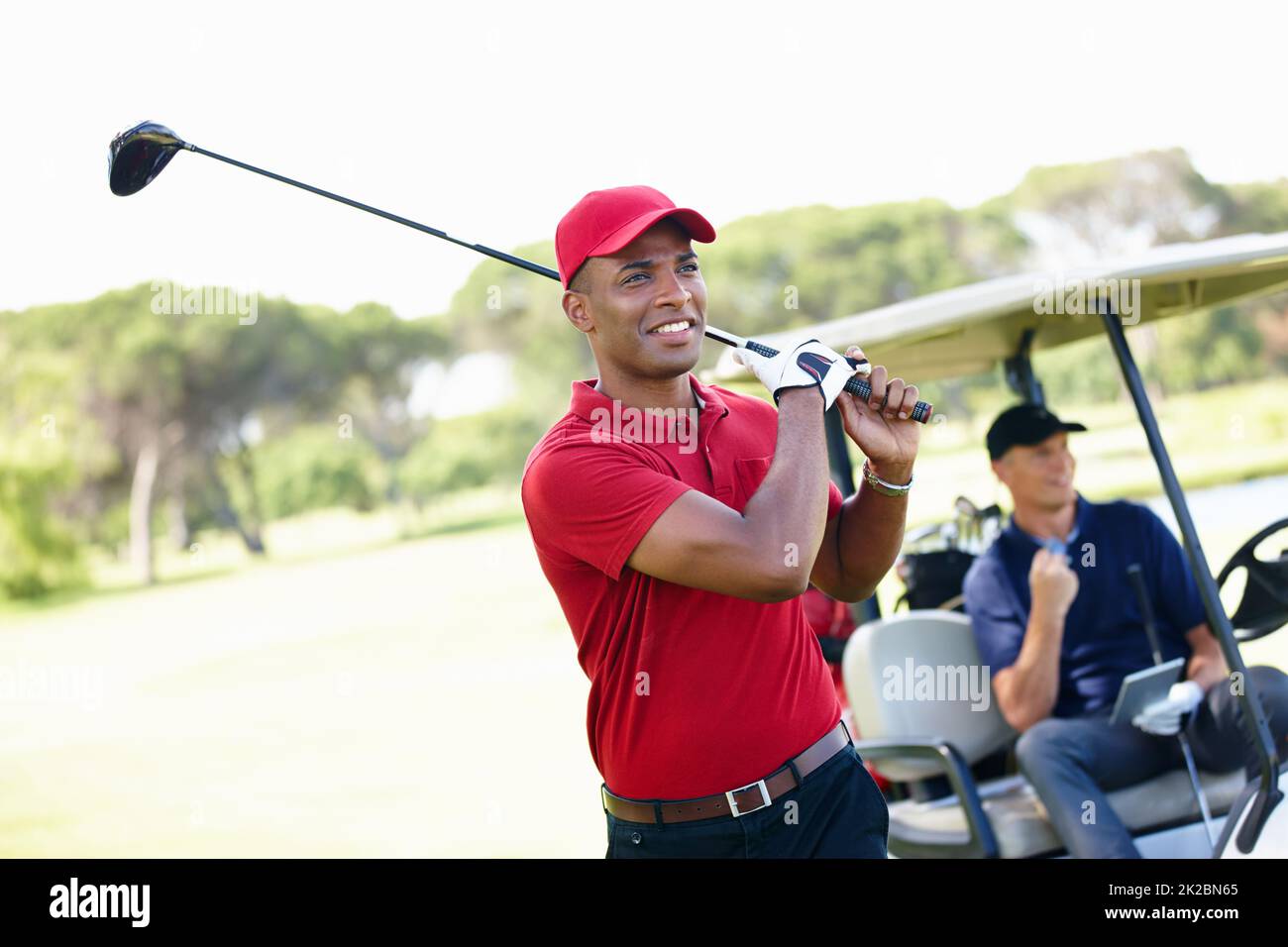 Das war gut. Aufnahme eines jungen Mannes, der einen Schuss gemacht hat, während sein Freund ihm vom Golfwagen im Hintergrund gratuliert. Stockfoto