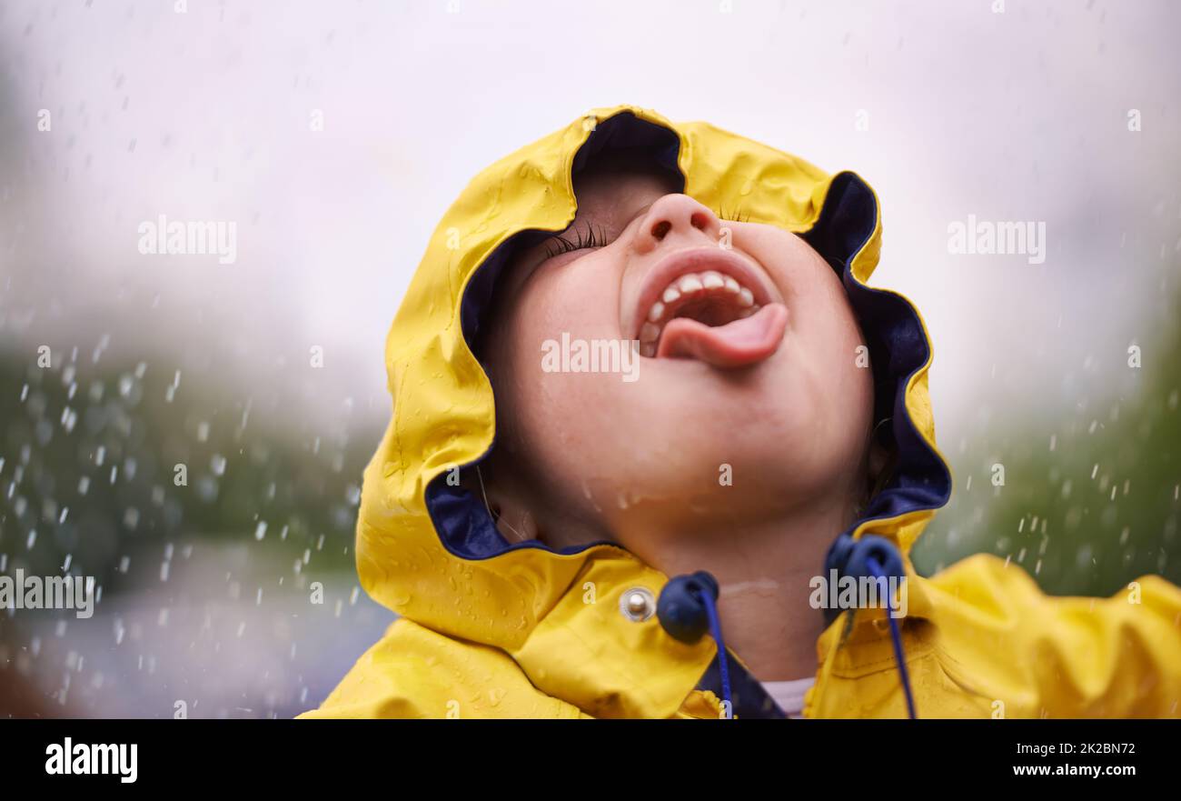 Um den Regenbogen zu genießen, genießt zuerst den Regen. Ein kleines Mädchen, das Spaß im Regen hat. Stockfoto