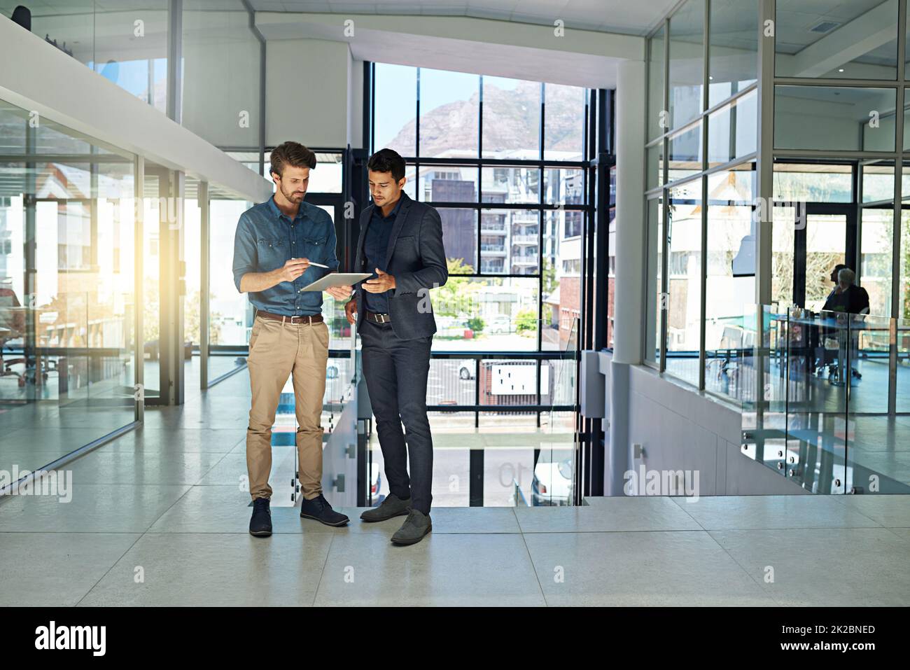 Sie arbeiten an allen großen Projekten zusammen. Aufnahme von zwei Kollegen, die sich über ein digitales Tablet unterhalten, während sie in einem modernen Büro stehen. Stockfoto