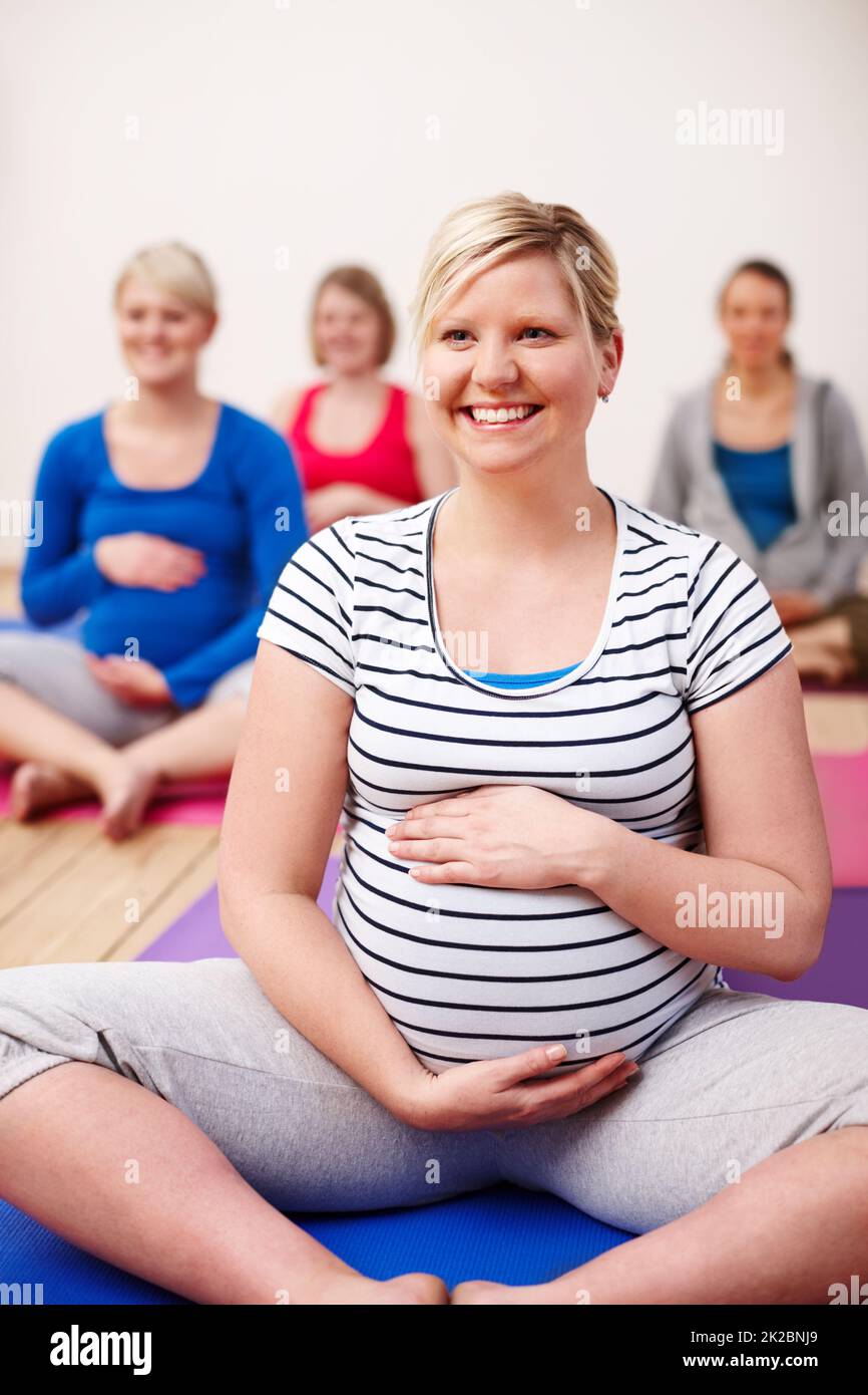 Mein Fokus liegt auf einer ruhigen Geburt. Eine Gruppe von Schwangeren, die in einem Yoga-Kurs mit gekreuzten Beinen sitzen und glücklich lächeln. Stockfoto