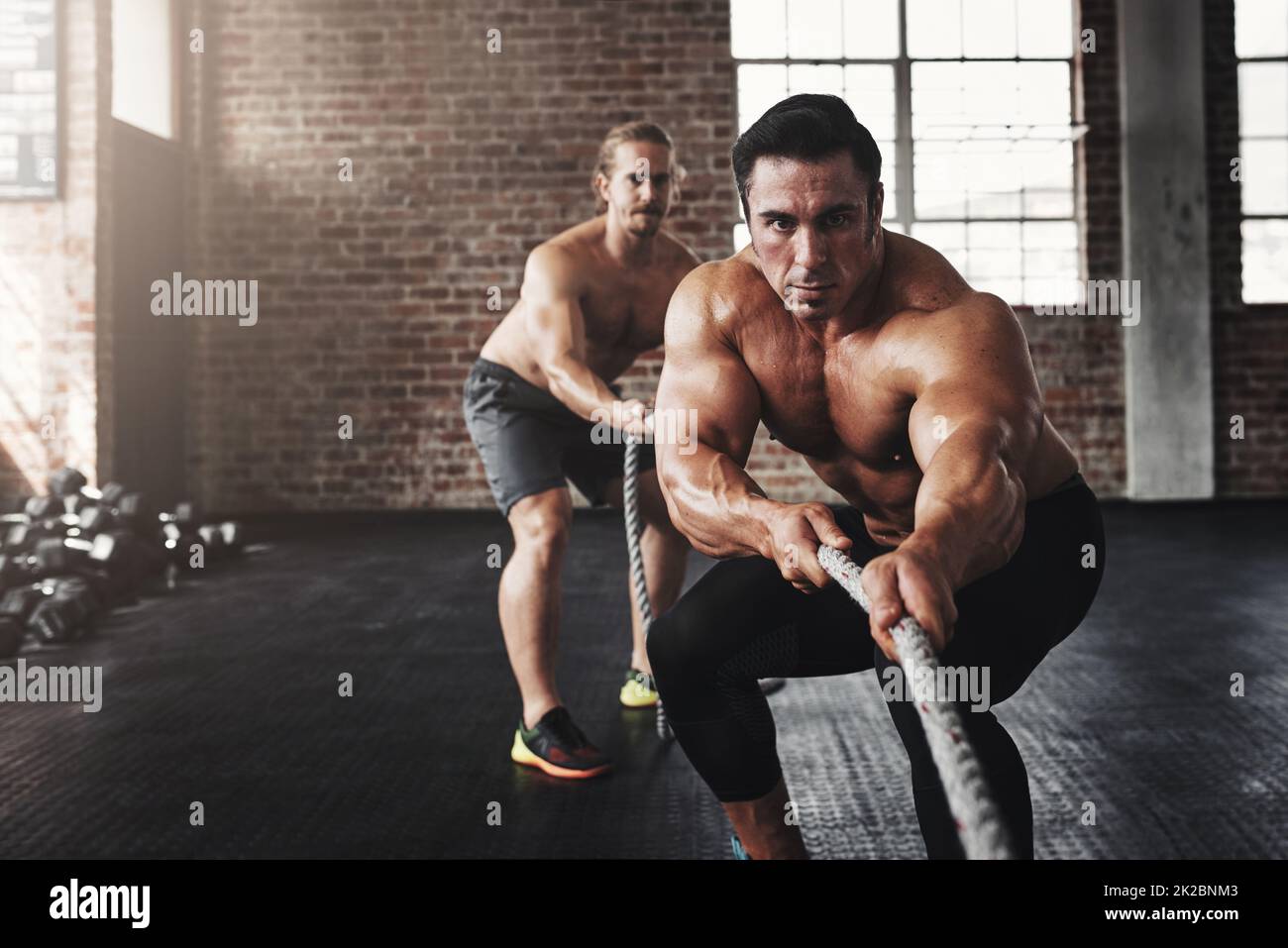 So sieht fit und wild aus. Aufnahme von zwei muskulösen jungen Männern, die in einem Fitnessstudio an einem Seil ziehen. Stockfoto