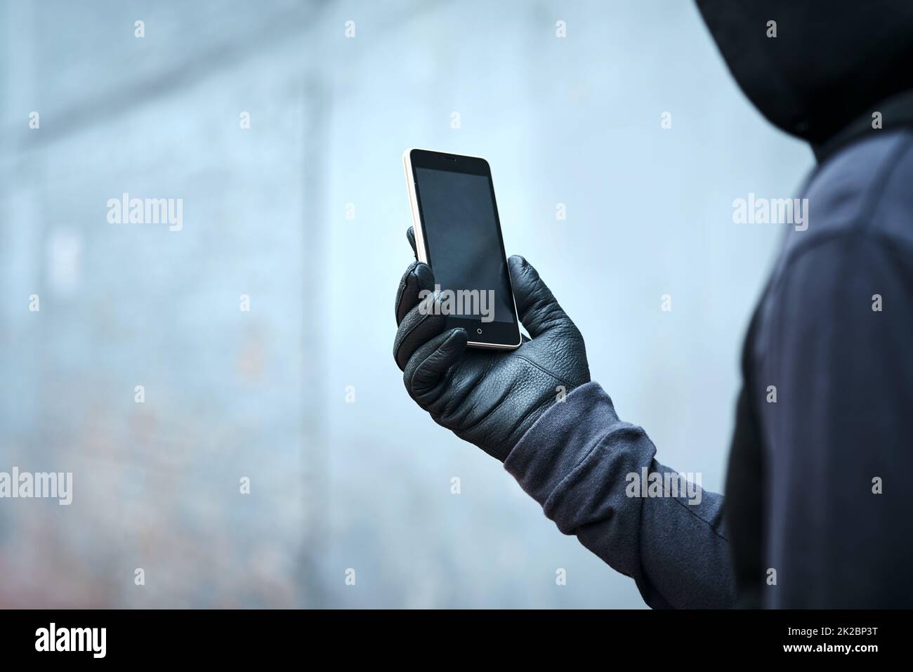 Einen kurzen Blick darauf werfen, wo als nächstes schlecht zuschlagen wird. Aufnahme eines männlichen Einbrechers, der sein Telefon im Freien benutzt. Stockfoto