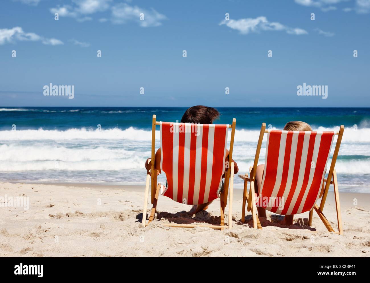 Nicht stören, im Urlaub. Rückansicht eines Paares, das auf den Liegestühlen am Wasserrand liegt. Stockfoto