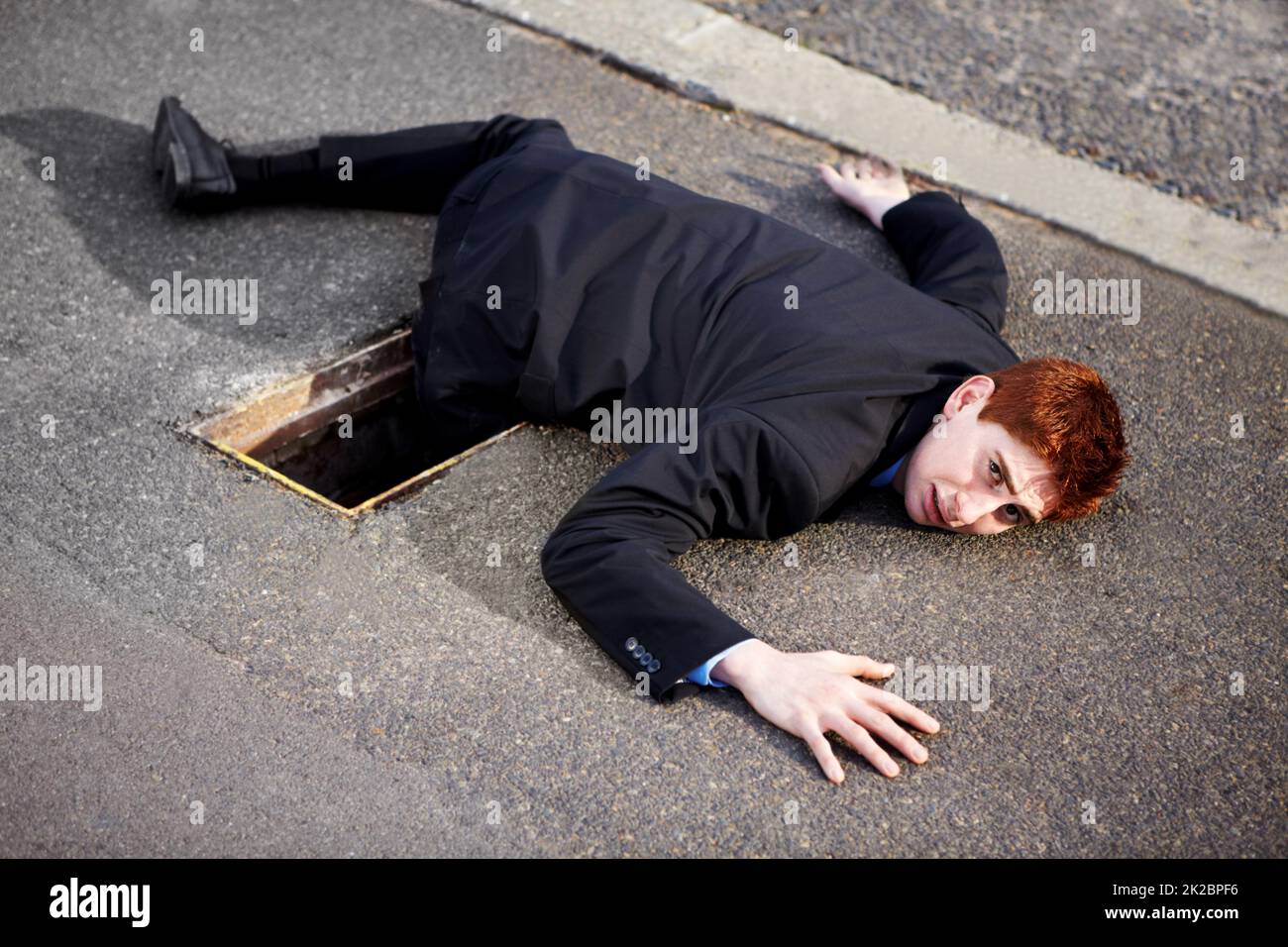 Auf dem Weg zum Erfolg gibt es viele Hindernisse. Ein junger Geschäftsmann, der auf dem Boden lag und sein Bein in einem Abfluss feststeckte. Stockfoto