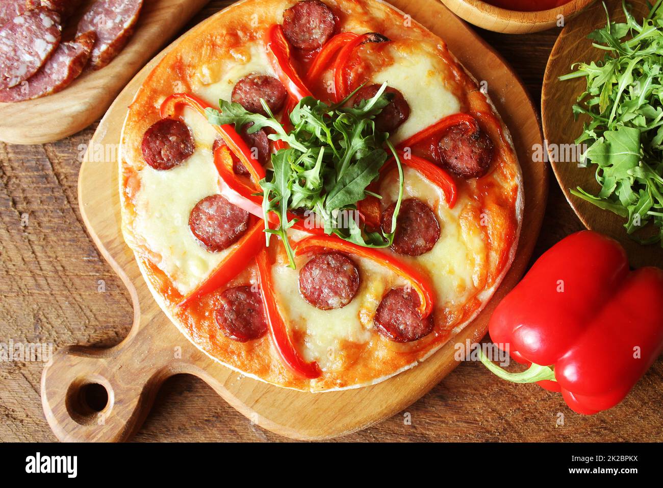 Hot hausgemachte Pizza mit Salami, paprica, Rucola auf hölzernen Tisch. Ansicht von oben Stockfoto
