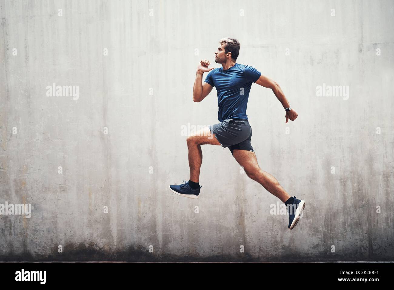 Halten Sie die Energie hoch. Aufnahme eines sportlichen jungen Mannes, der draußen gegen eine graue Wand läuft. Stockfoto