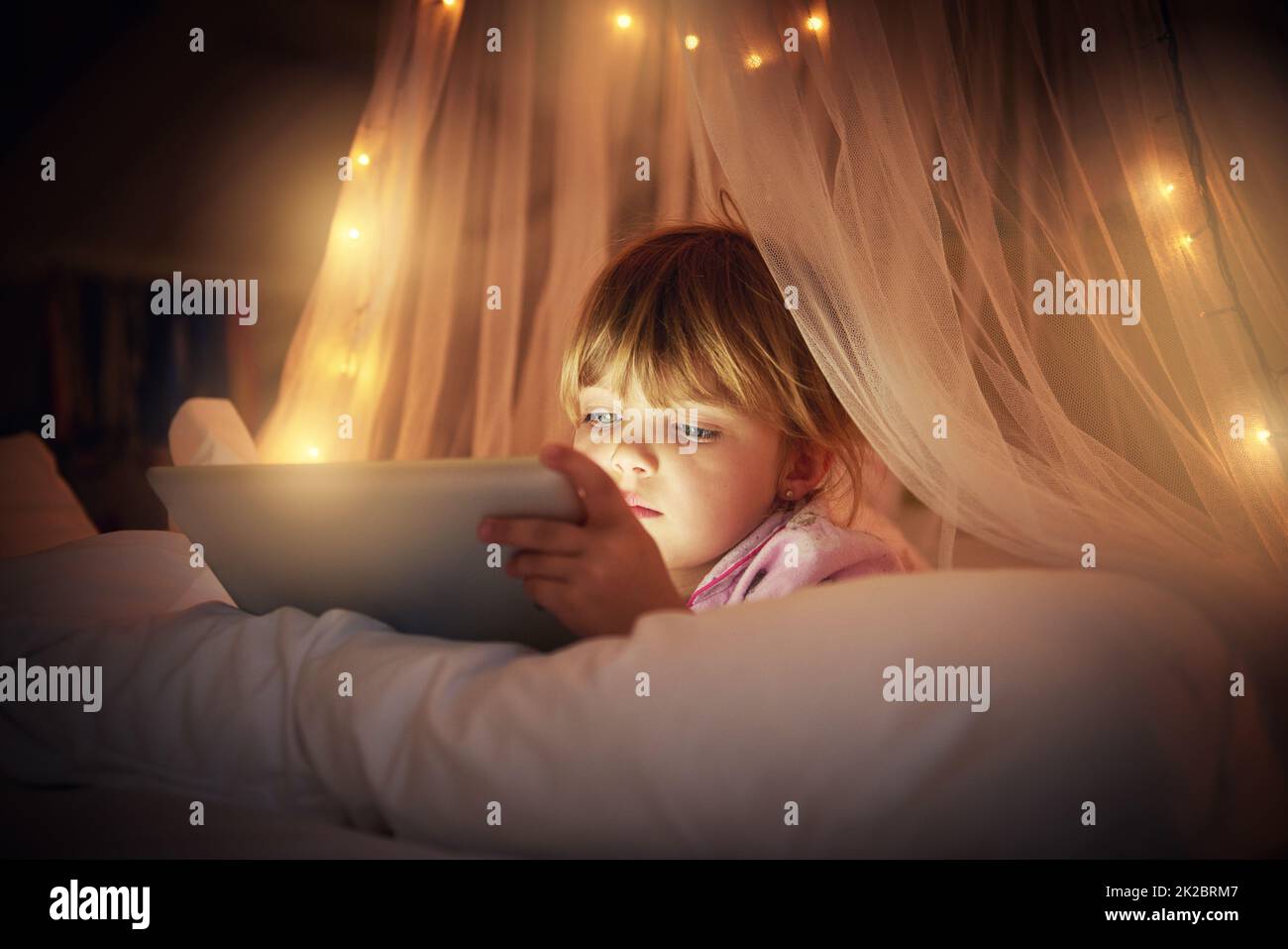 Eine Pause von den Geschichten aus dem Schlafengehen für die Mutter. Ein junges Mädchen liegt auf ihrem Bett, während es ein digitales Tablet benutzt. Stockfoto