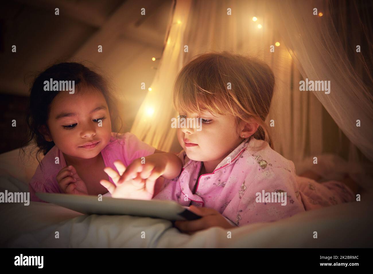 Es ist an der Zeit für eine magische Schlafenszeit. Aufnahme von zwei kleinen Mädchen, die ein digitales Tablet bei ihrem Sleepover benutzten. Stockfoto