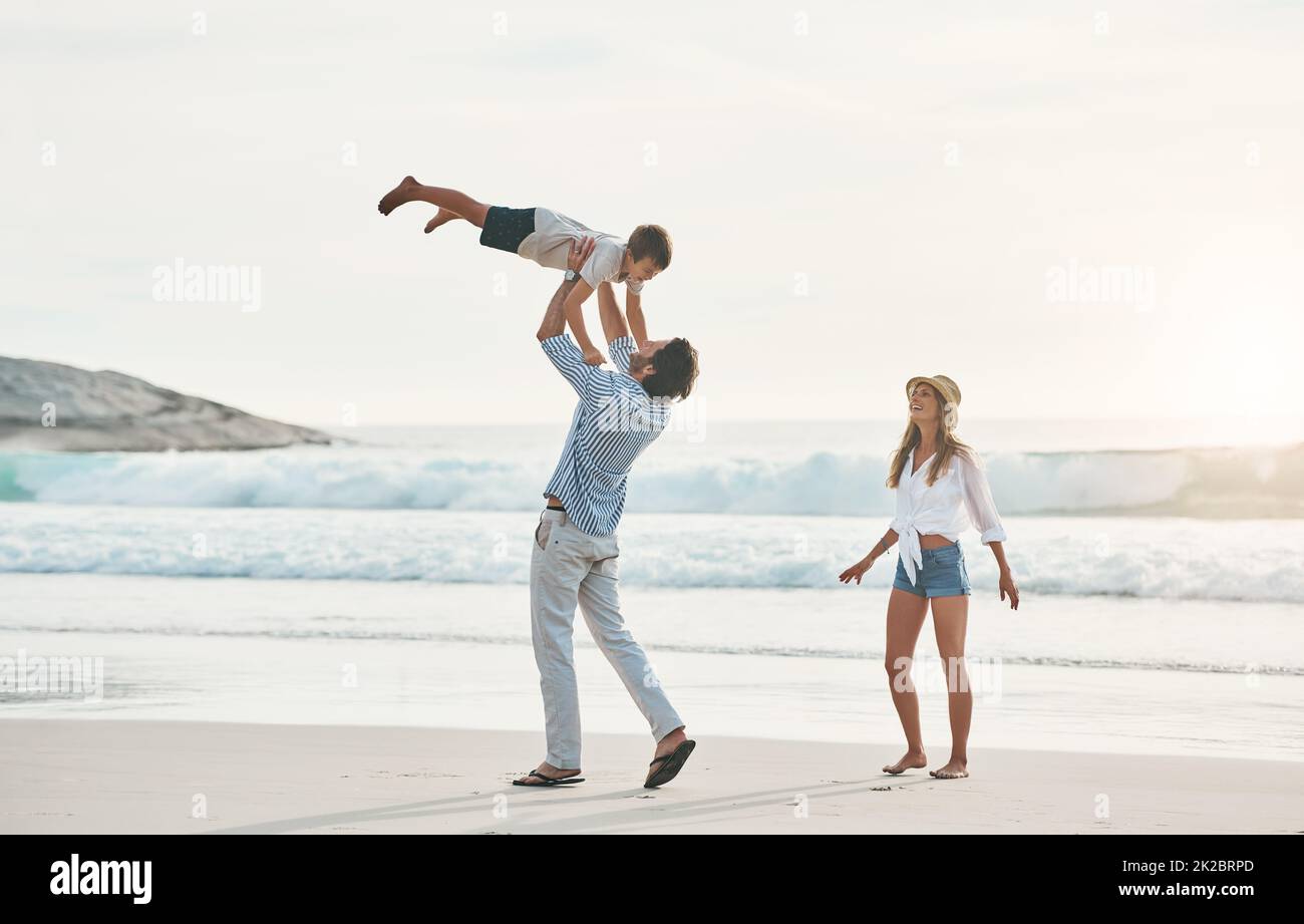 Eins, zwei, drei, hoch geht's. Ganzkörperaufnahme eines glücklichen jungen Paares, das sich während eines schönen Tages am Strand mit ihrem jungen Sohn freundlichmacht. Stockfoto