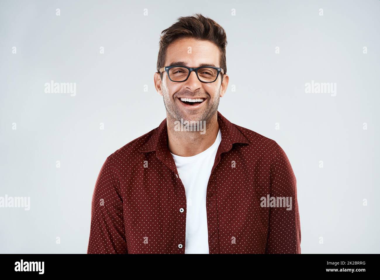 Lustig und intelligent. Porträt eines fröhlichen jungen Mannes, der eine Brille trägt und hell lächelt, während er vor einem grauen Hintergrund steht. Stockfoto