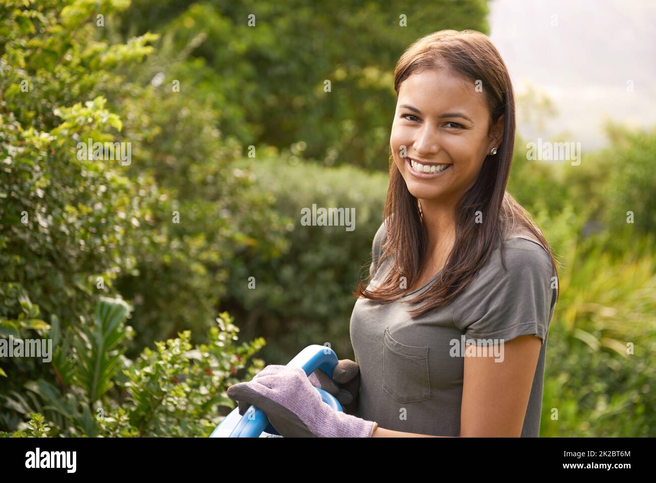 Umgeben von Naturschönheiten. Aufnahme einer attraktiven jungen Frau, die ihren Garten bewässert. Stockfoto