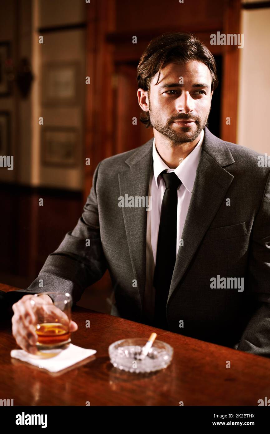 Er ist ein cooler Kunde. Ein gut gekleideter junger Mann, der bei einem Drink an einer Bar sitzt. Stockfoto