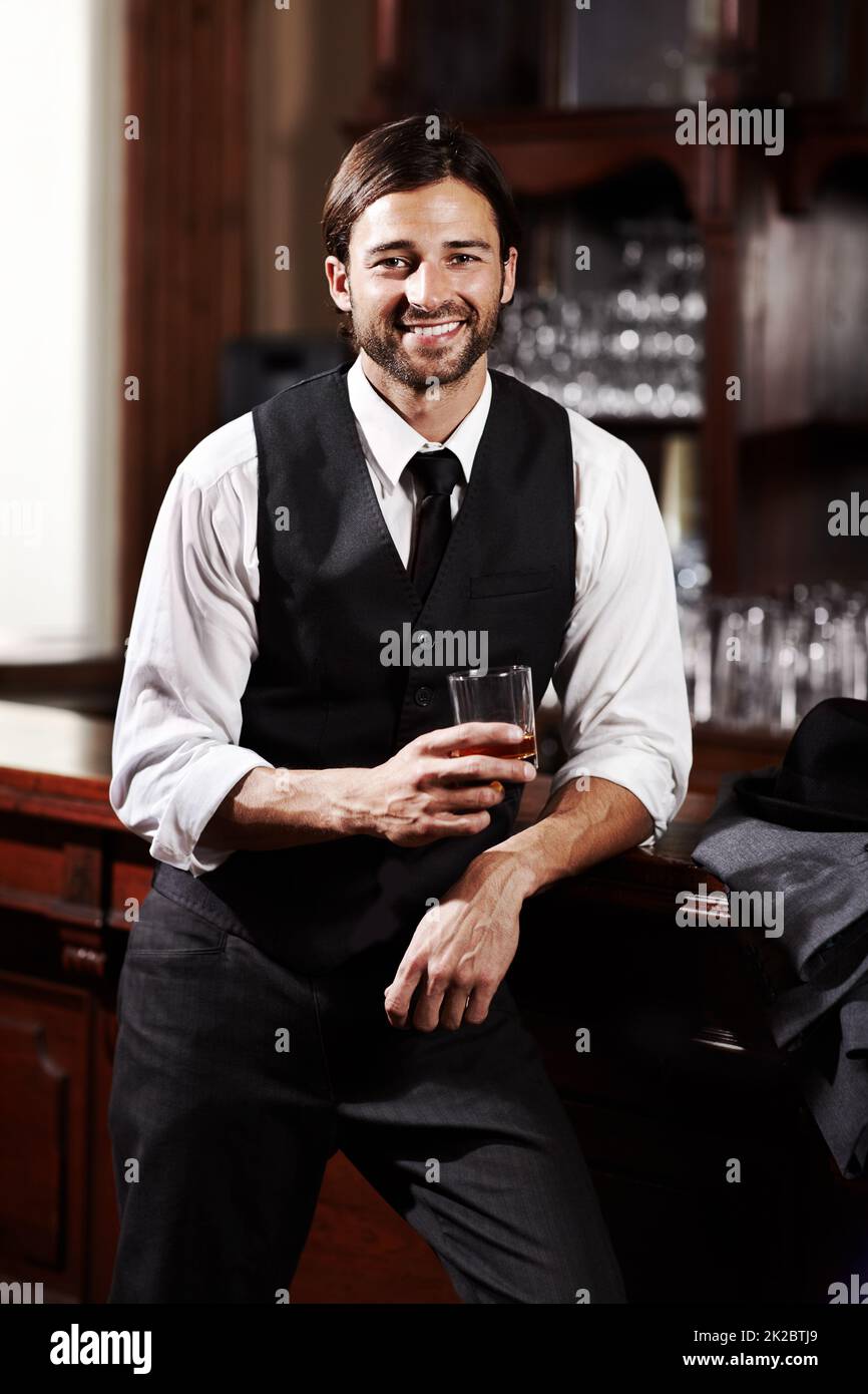 Entspannen bei einem Drink. Porträt eines gut gekleideten jungen Mannes, der bei einem Drink an einer Bar steht. Stockfoto