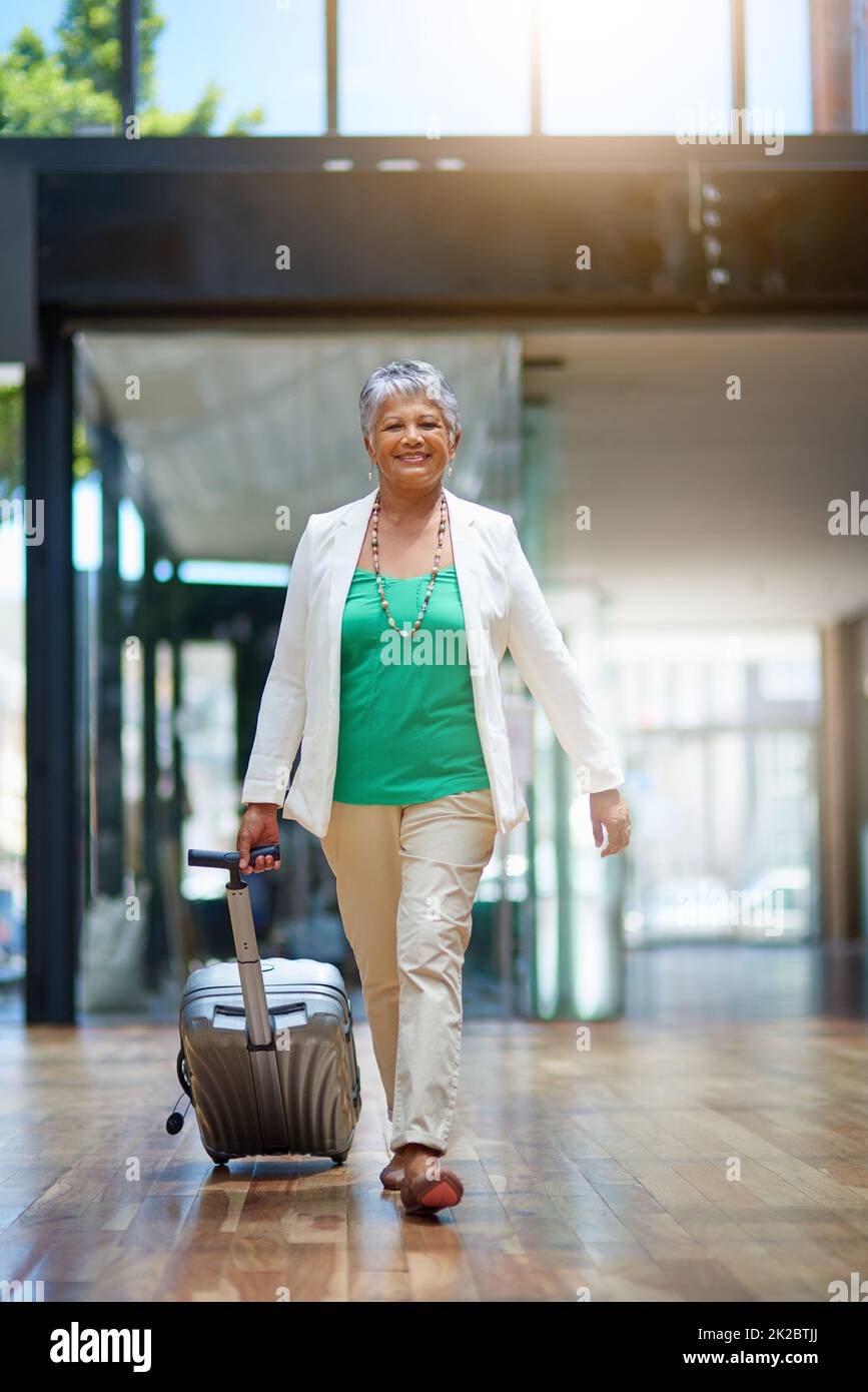 Auf ihrem Weg, die Welt zu sehen. Aufnahme einer reifen Frau, die mit ihrem Koffer in einem Flughafenterminal läuft. Stockfoto