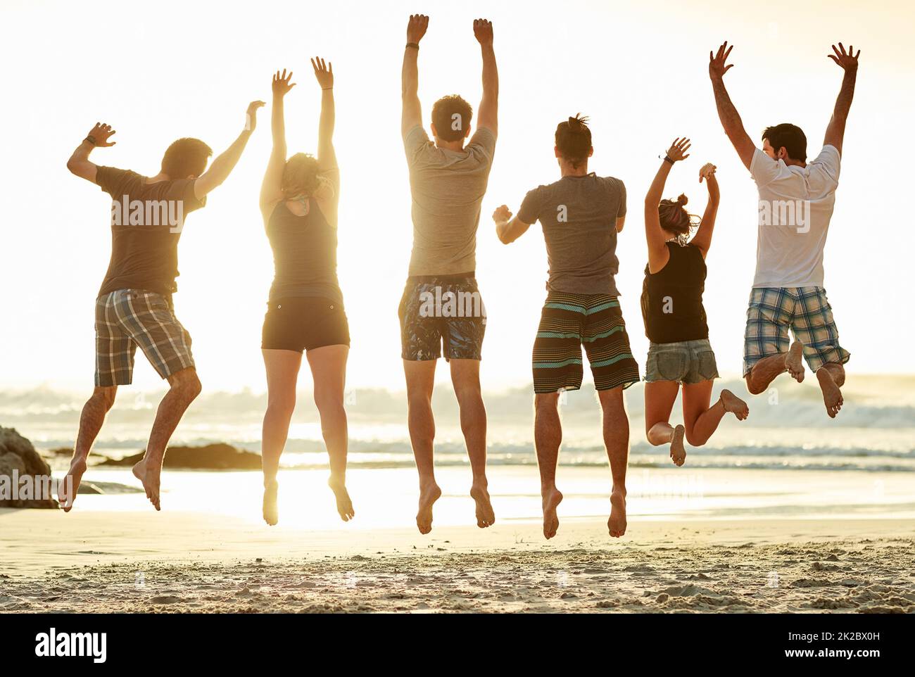 Luftholen am Strand. Rückansicht einer Gruppe von nicht identifizierbaren Freunden, die bei Sonnenuntergang am Strand zusammenspringen. Stockfoto