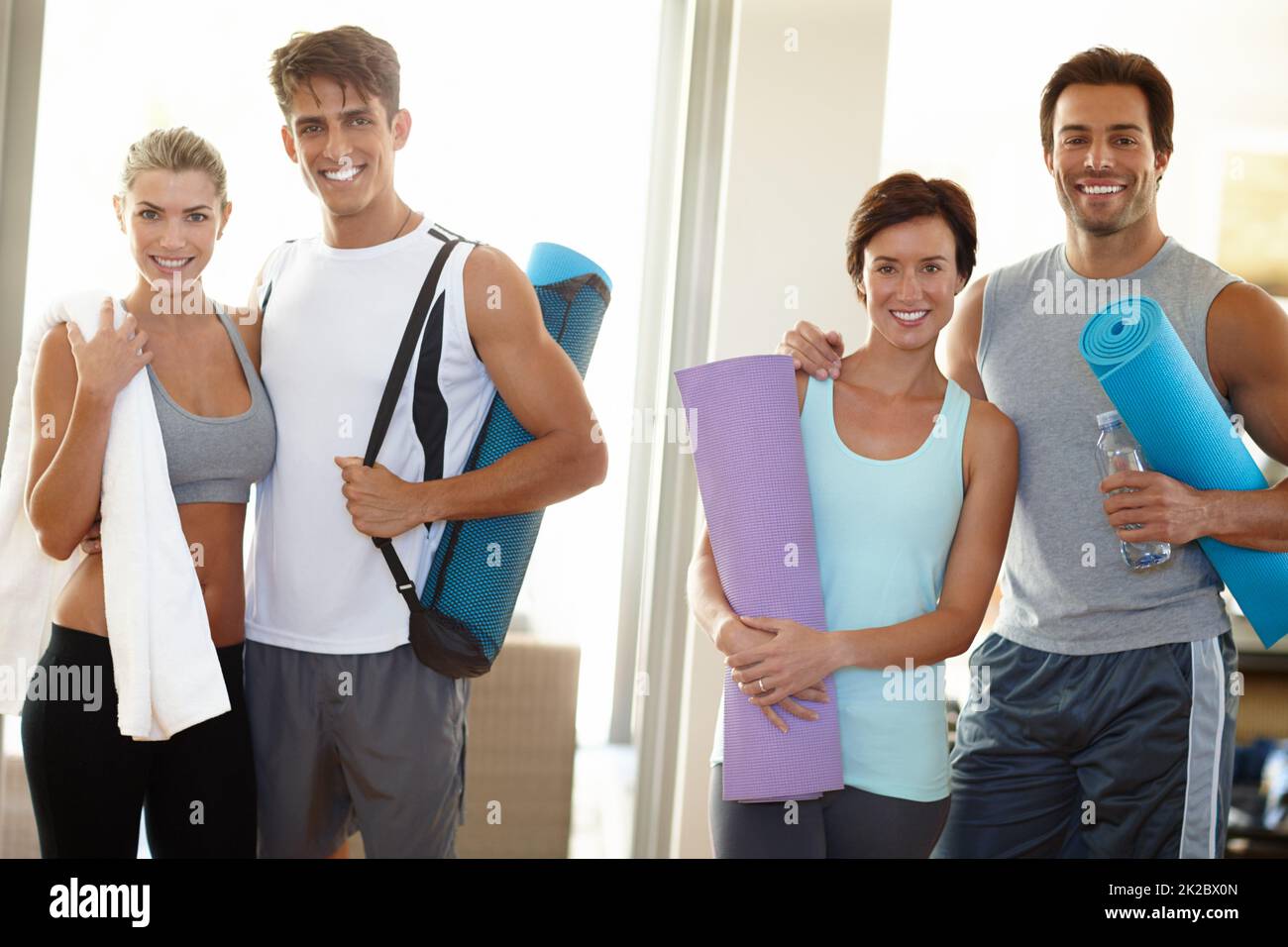 Teil eines Fitness-Teams. Porträt von vier jungen Erwachsenen, die mit ihrer Yoga-Ausrüstung lächeln. Stockfoto