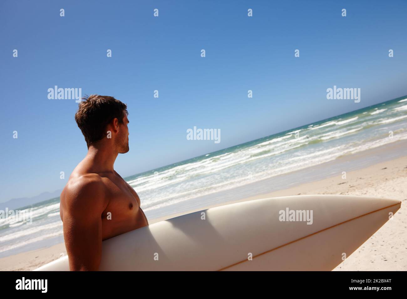 Surft auf. Kopf- und Schulteraufnahme eines jungen Mannes, der mit seinem Surfbrett am Strand steht. Stockfoto