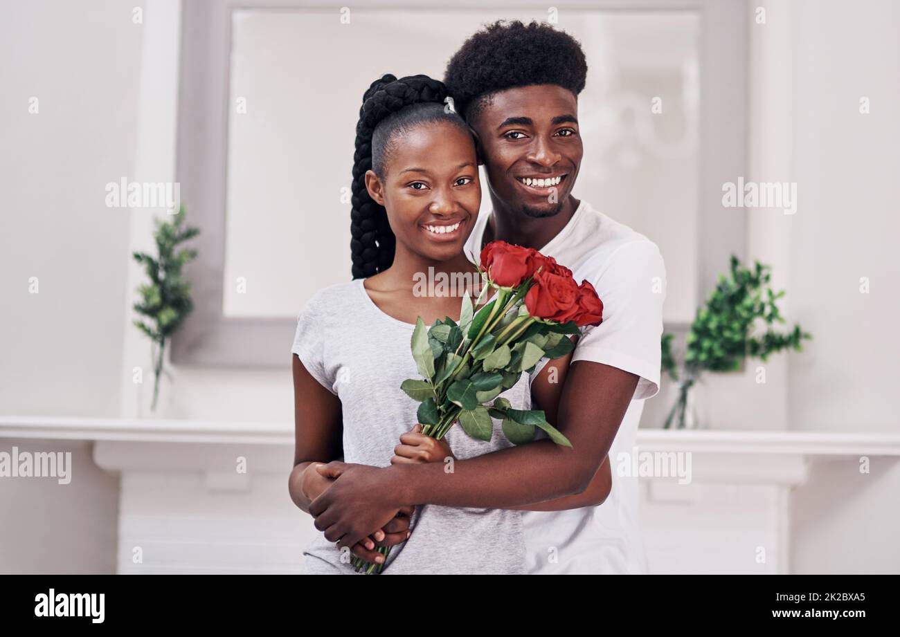 Die Auszeichnung für das Paar des Jahres geht an Aufnahme einer jungen Frau, die ein paar rote Rosen in der Hand hält, während sie mit ihrem Freund zu Hause steht. Stockfoto