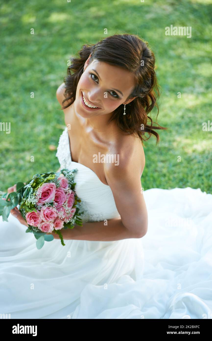 Strahlend an ihrem großen Tag. Eine wunderschöne Braut, die auf Gras sitzt. Stockfoto