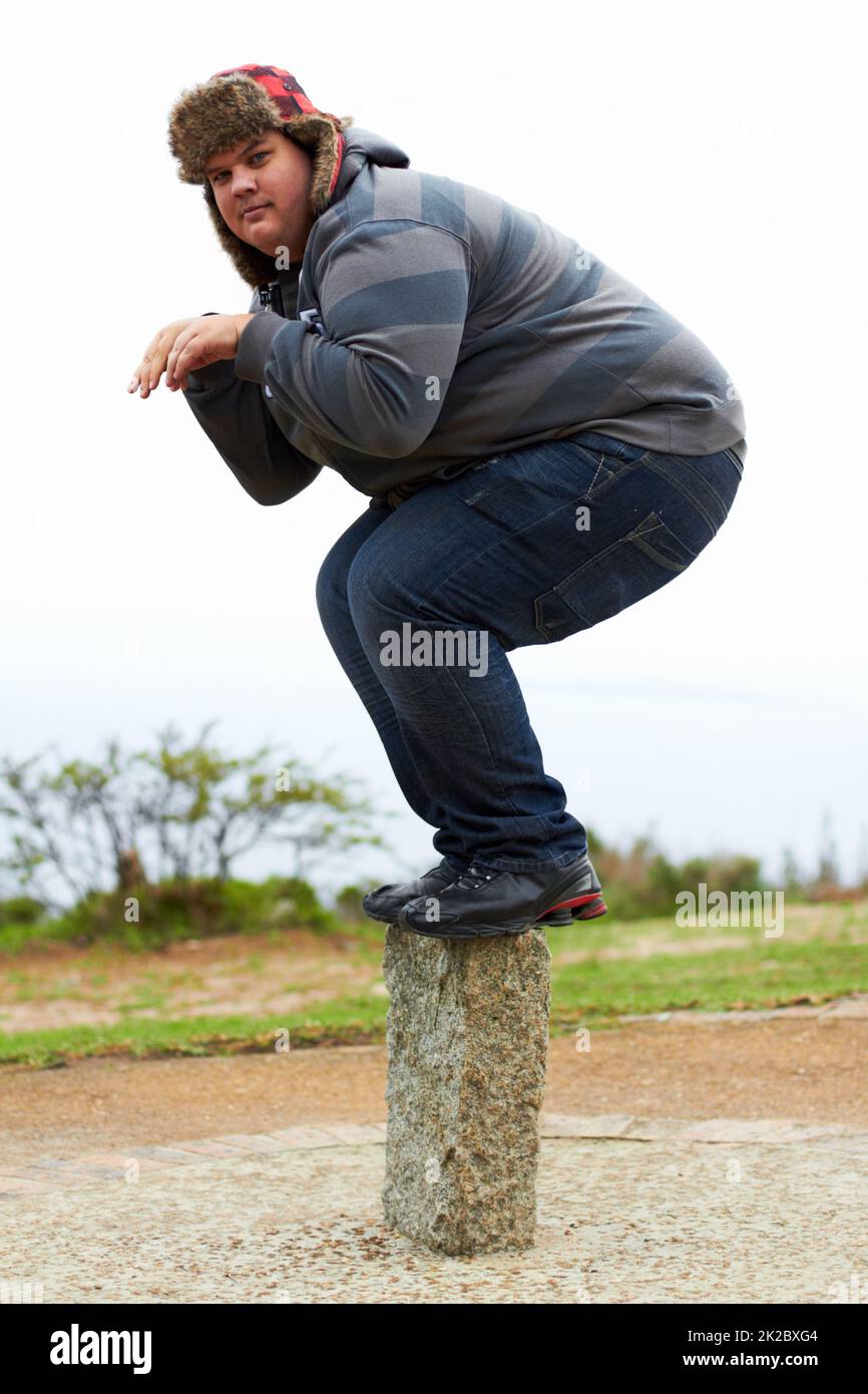 Bereit zum Stunzen. Ein übergewichtiger junger Mann im Winter trägt spielerisch auf einem Posten balanciert. Stockfoto