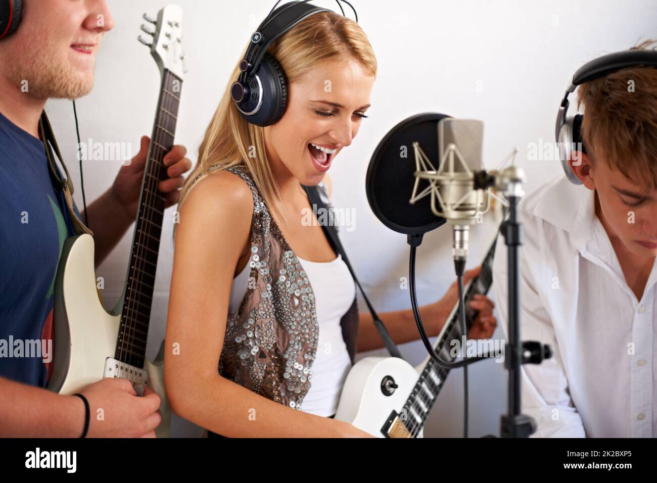 Rockt aus. Eine schöne junge blonde Frau singt, während ihre beiden Bandmitglieder im Hintergrund Musik machen. Stockfoto